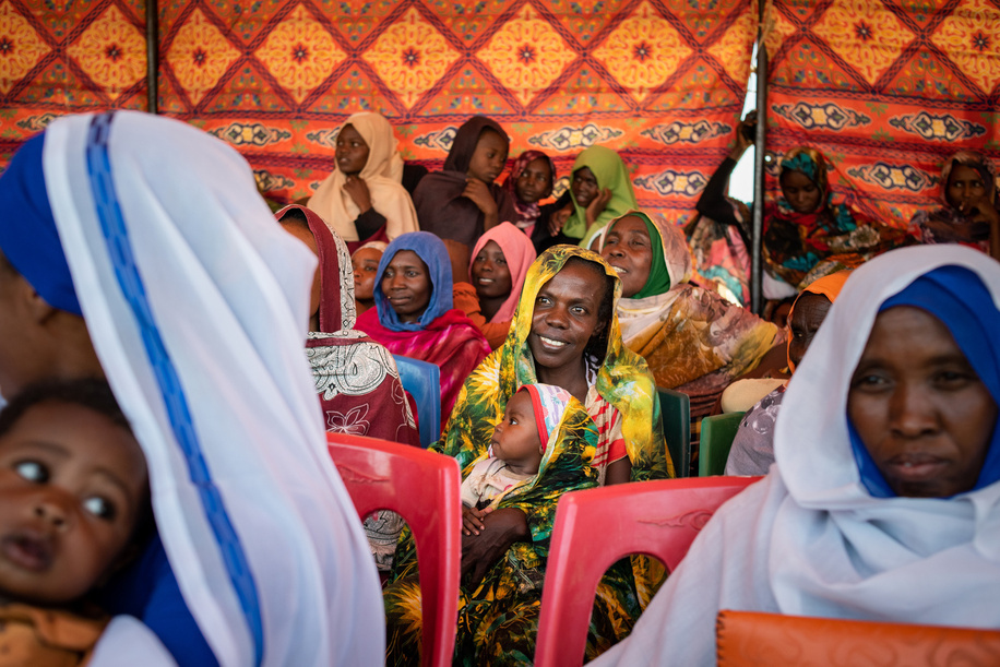 North Darfur, Sudan - 25 April 2022: Women from Abu Gaw listen to speeches during a celebration to mark the opening of the village’s new health care centre. Prior to its construction, people from Abu Gaw had to travel long distances to reach health services, but many couldn’t afford the cost of transport. Their previous health care centre was destroyed and residents of Abu Gaw fled from their village during the war in Darfur in 2004. Since 2018, about 8000 people have returned to the village from displacement camps. The community identified rebuilding the health centre as a priority through a series of community health dialogues facilitated by the WHO with North Darfur health authorities. Community dialogues empower disadvantaged populations to take an active role deciding on their health priorities, proposing solutions for their health needs, and holding local health authorities accountable. The dialogues in Abu Gaw provided guidance for the community about how and where to advocate for the health services they needed most. Community leaders identified a local nongovernmental organization, Africa Humanitarian Action (AHA) to build the facility. UNHCR supported the project with funding from the government of Denmark. The Ministry of Health is overseeing the operation and staffing of the health centre, and WHO is providing equipment, medicines and staff training. Sudan is one of the 115 countries and areas supported by the Universal Health Coverage Partnership, WHO’s largest platform for international cooperation on delivering universal health coverage through a primary health care approach. Primary health care-oriented health systems maximize the quality of the health system, while also enhancing equity and solidarity, thus improving social cohesion. With 2.5 million internally displaced people (IDPs) in Sudan, there is an urgent need to strengthen basic services and build community resilience so that people can return home and live in peace.
