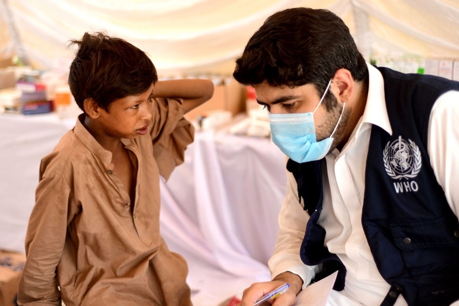 WHO District Surveillance Officer Dr Nauman Khan checks on a boy who was displaced by the floods at a medical tent in a makeshift camp in Charsadda Sports Complex on 31 August 2022. Catastrophic floods in Pakistan in August 2022 killed some 1,400 people, destroyed more than half a million homes and displaced over 660,000 people into camps. Many more people are displaced in host communities. More than 750,000 livestock – a critical source of income for many families – died after the rainfall, which in August was more than five times the national 30-year average in some parts of Pakistan. According to the Food and Agriculture Organization, the floods damaged 1.2 million hectares of agricultural land in Sindh Province alone. Some 33 million people have been affected, and access to many vulnerable communities was cut off as hundreds of bridges and thousands of kilometres of roads were destroyed or washed away.  WHO is supporting the Government of Pakistan to respond by delivering supplies needed by health facilities and increasing disease monitoring to prevent the spread of infectious diseases. https://www.who.int/emergencies/situations/pakistan-crisis