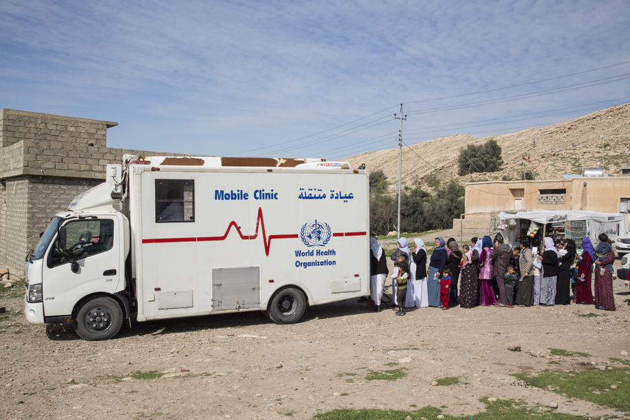 WHO Mobile Clinic in Duhok - Every month a WHO supported mobile health clinic visits Sienna village, close to the Sharia collective town in the Duhok region of northern Iraq. About 1,500 Yazidi live in the village, many of them in unfinished buildings. They’ve been displaced from Sinjar mountain since 2014. The medical staff, which consists of a doctor, two nurses, a pharmacy assistant, a nurse practitioner and a driver, typically sees between 100-150 patients each visit. WHO supports six mobile clinics in the region and they serve about 40,000 people who do not live in camps. Four are wholly supported by WHO and two run by the national NGO Heevie have a separate operation with vehicles donated by WHO. The Duhok Directorate of Health also contributes to the clinics. They visited Sumer Zahko, Amedi and Shikhan districts. Because of the financial constraints facing the Kurdish region, which mean many public servants are not receiving their full salary, four of the mobile teams receive a monthly financial incentive of $1,000 for doctors and $550 for nurses. - Yezidi men, women and children line up at a Mobile Clinic to get medical attention.