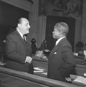 Dr Marcolino G. Candau (left), Director-General of the World Health Organization talks with Dr Joseph N. Togba, after his election as President of the Seventh World Health Assembly. Title of WHO staff and officials reflects their respective position at the time the photo was taken.